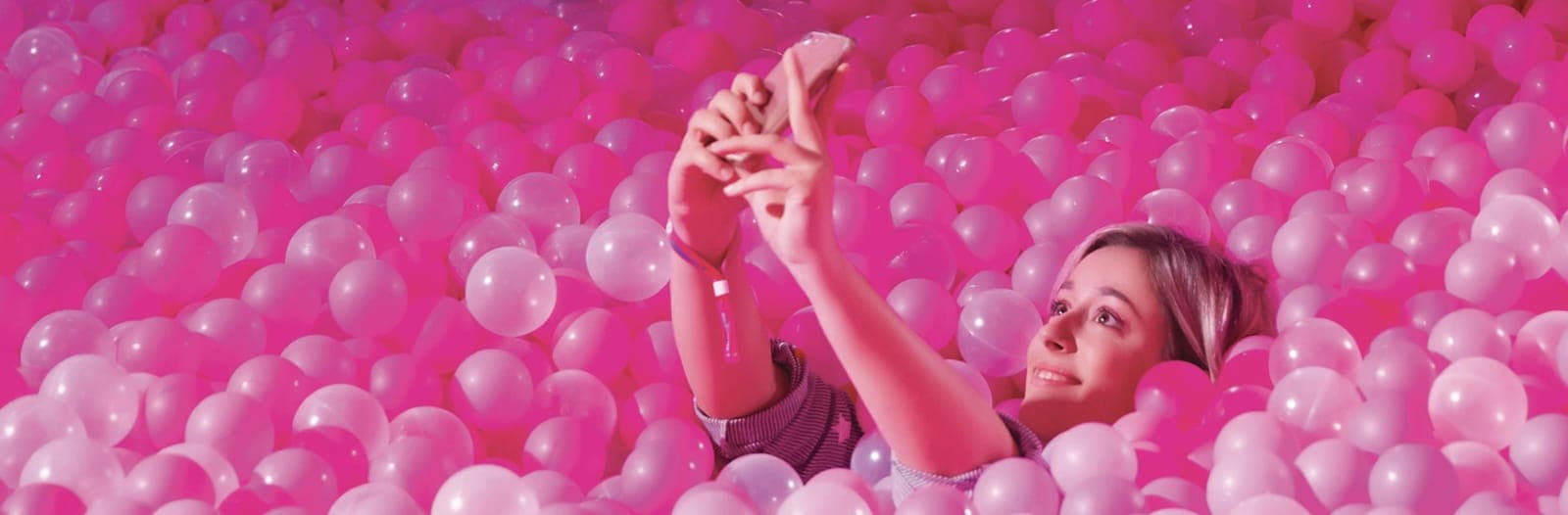 A woman takes a selfie lying in a pit of pink balls