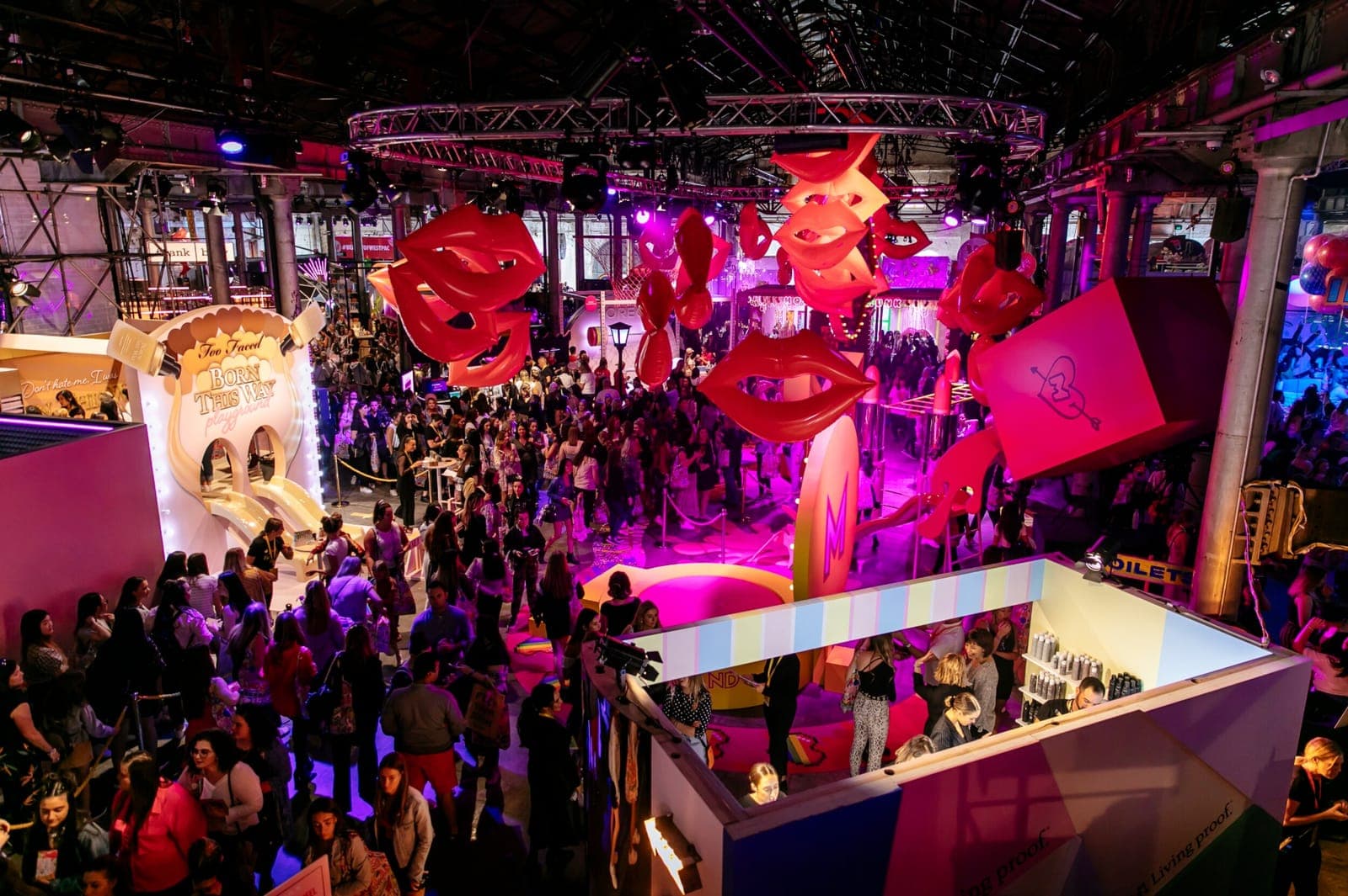 Crowds fill the festival floor beneath giant red lips and brand booths