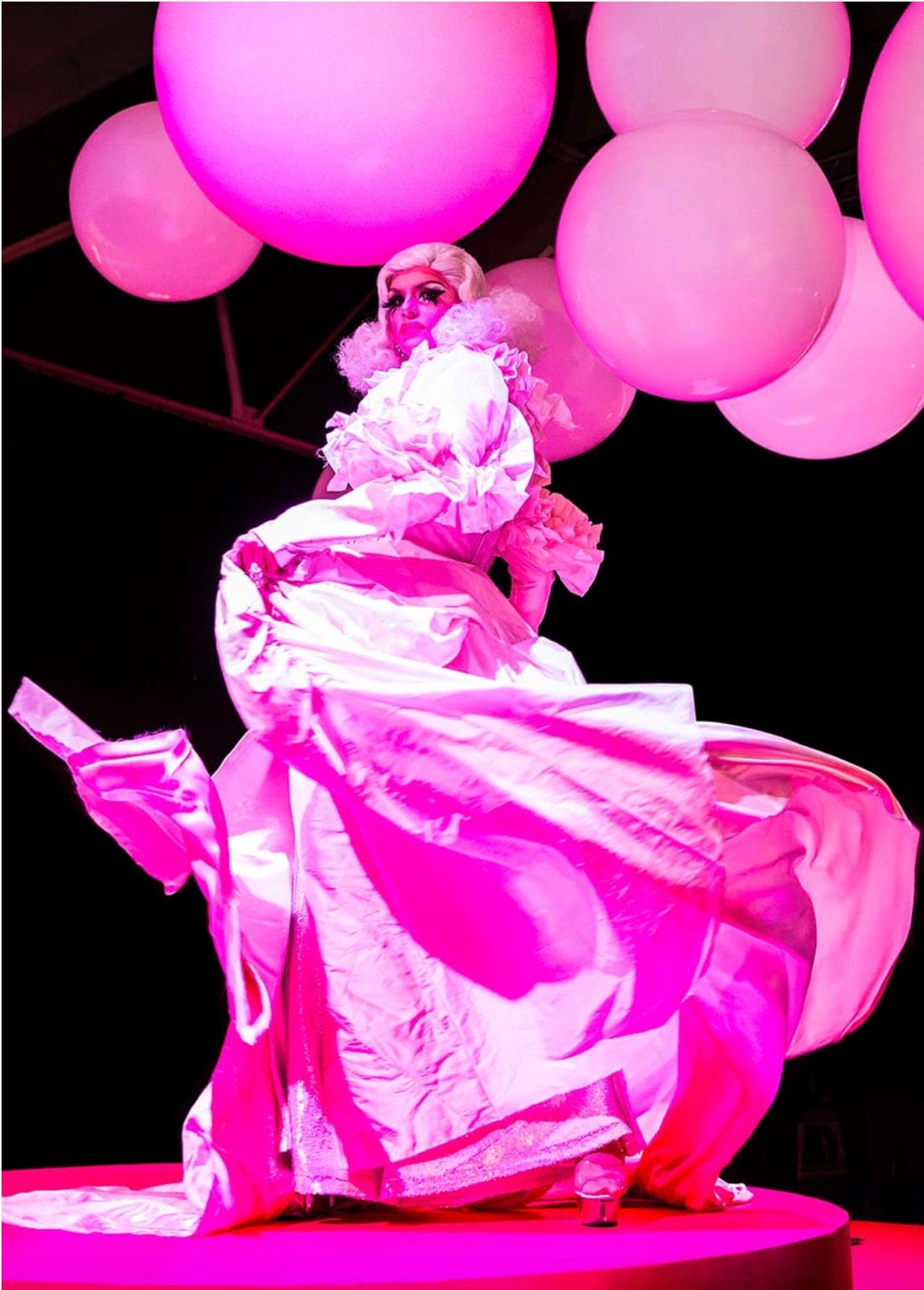 A performer in a billowing pink gown under giant pink balloons