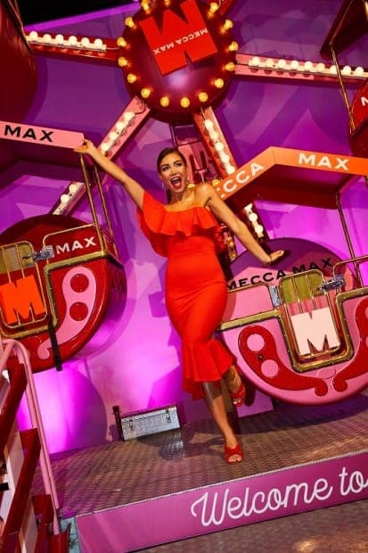 A woman in a red dress poses on a MECCA MAX stage