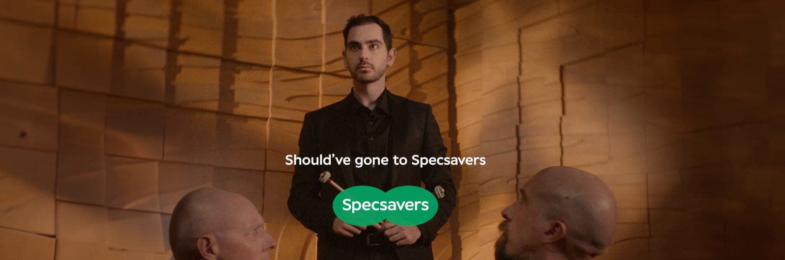 End frame: the percussionist holds his mallets between two orchestra members above the line Should’ve gone to Specsavers and the Specsavers logo