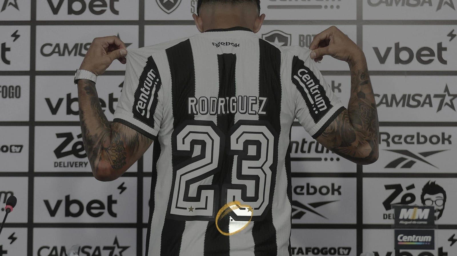Rodriguez holds up his number 23 shirt at a press wall, the dot circled in gold
