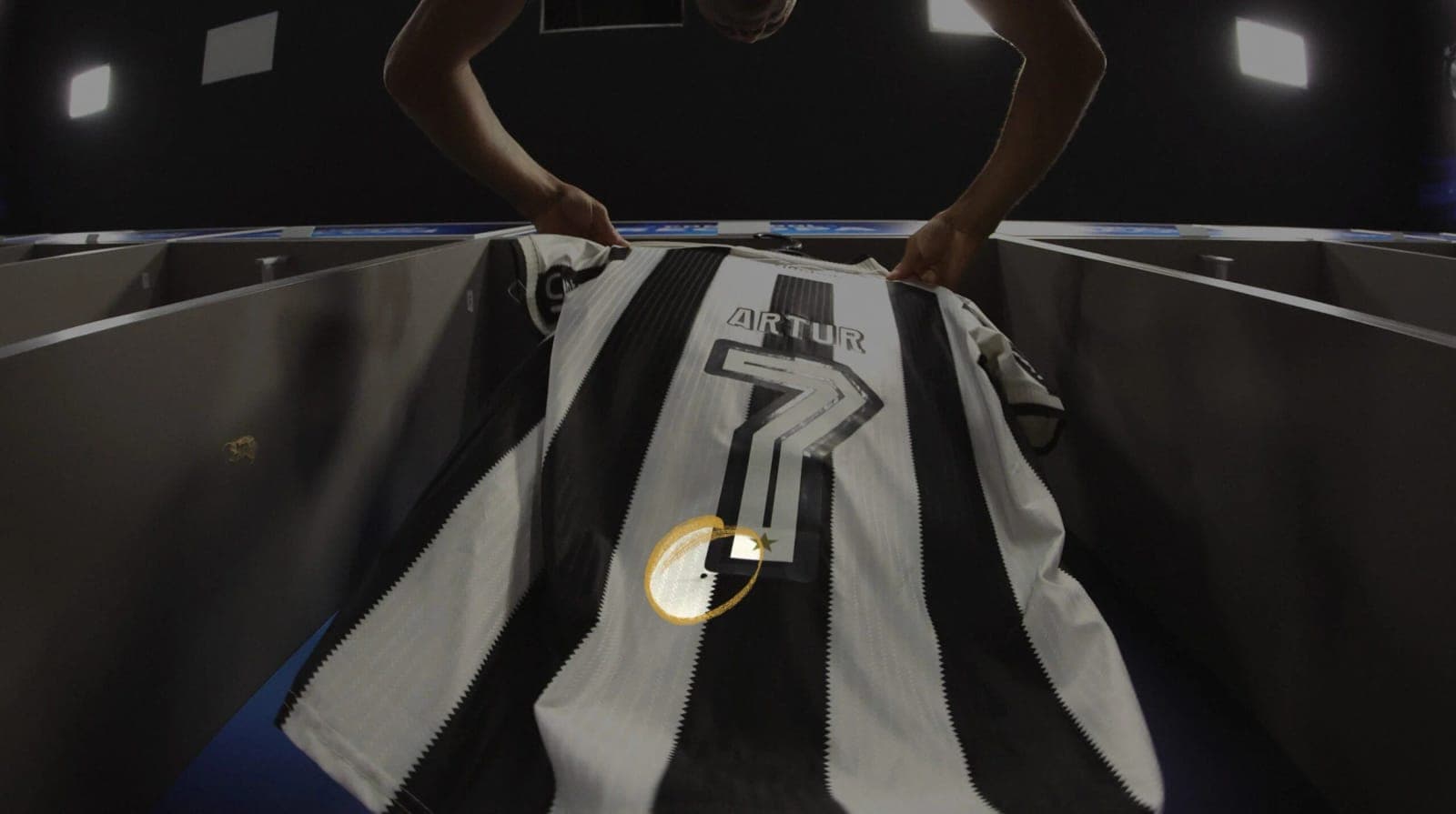 Hands lifting Artur’s number 7 shirt in a dressing room, the dot circled in gold